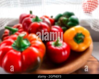Blurred. Fresh harvest. Multi-colored textured peppers lie on a wooden plate against the background of the window. Colorful sweet bell peppers, natura Stock Photo