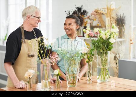 Portrait of smiling senior man talking to young woman in flower shop Stock Photo