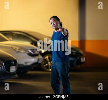 Asian long hair man stands and posts in parking car with orange yellow light behind. Stock Photo