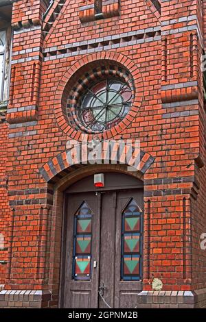The entrance to the old red brick building. A wooden door with colored panels and a round stained-glass window above the entrance. Russia. Kaliningrad Stock Photo