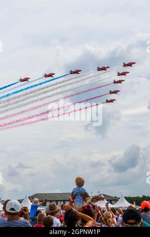 Young child being held up high to watch the RAF Red Arrows display team pass in a arrow shape flypast at Farnborough, UK. Small boy aviation fan Stock Photo