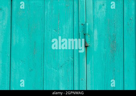 A fragment of an old wooden door of blue or turquoise color on rusty hinges Stock Photo