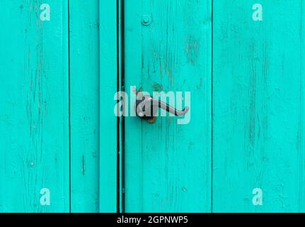 A fragment of an old wooden door of blue or turquoise color with a curly handle Stock Photo