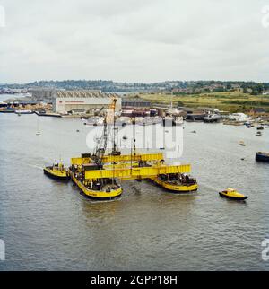 A twin hull barge being towed down river from Woolston, Hampshire, for use in the construction of the Peel Common Sewage Works outfall at Browndown. Laing Civil Engineering were contracted to construct the Browndown Outfall for the Southern Water Authority, as part of the South Hampshire Main Drainage Scheme for the treatment and disposal of sewage. Browndown Outfall is a 1km long underwater culvert which transports treated sewage from Peel Common Sewage Works, another contract carried out by Laing. The outfall was built in sections which were linked together in a chain on the seabed. The land Stock Photo