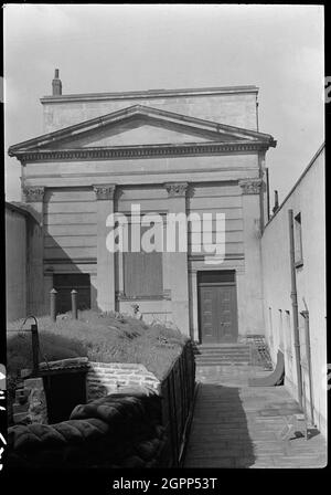 Chapel at Hull Trinity House and statue outside east front, Princes Dock Street, Kingston upon Hull, 1941. An exterior view of the east elevation of Trinity House Chapel, with a partial view of a sculpture of Oceanus and a bomb shelter in the foreground. The chapel dates to 1842, and was built by H. F. Lockwood. The east elevation is rusticated and has four giant Corinthian pilasters supporting a plain frieze and pediment, with the east window in the centre. Flanking the window are pairs of eight-panelled doors with stone pilasters and rectangular overlights. In front of the east window is a s Stock Photo