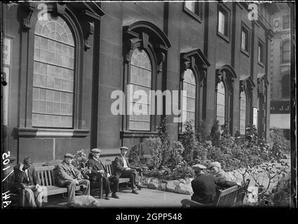 Holy Trinity Church, Boar Lane, Leeds, 1941. An exterior view of the Holy Trinity Church, showing the south front with men sat on benches in the foreground. The church was built between 1721 and 1727 by William Etty. The upper tower was added after 1839 by R. D. Chantrell. It has a rectangular plan with seven by three bays, with a tower in the middle bay of the west end. The south front has a door in the first bay, windows with alternating triangular and segmental pediments on the ground floor, and a second tier above. Stock Photo