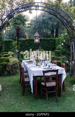 Table and chairs with lit candles under pergola in garden on the shores of Lake Garda Stock Photo