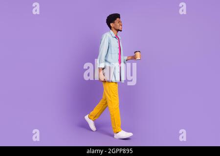 Photo of funky cute man wear denim walking drinking tea looking empty space holding gadget isolated purple color background Stock Photo