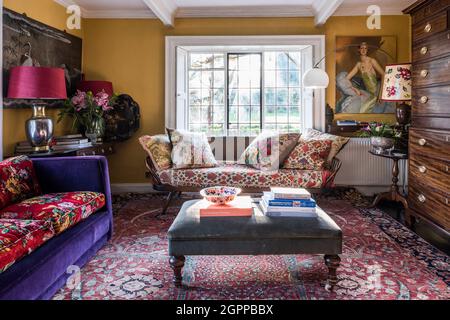 Mahogany tallboy and Ercol daybed with mix of bold colours and fabrics in Suffolk living room. Stock Photo
