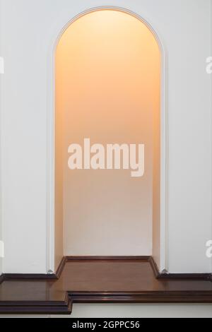 An arch-shaped wooden niche, lit from above, and brown on the bottom Stock Photo