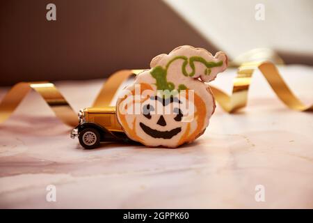Halloween decors with orange pumpkin mug, handmade cookie, felted pumpkins and yellow retro car. Happy Halloween festive concept. High quality photo.  Stock Photo