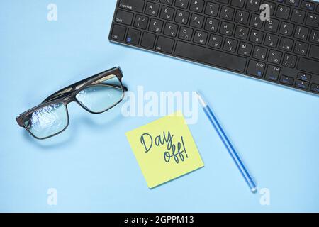 Eyeglasses, keyboard, pen and a sticker with a day off text on the blue surface Stock Photo
