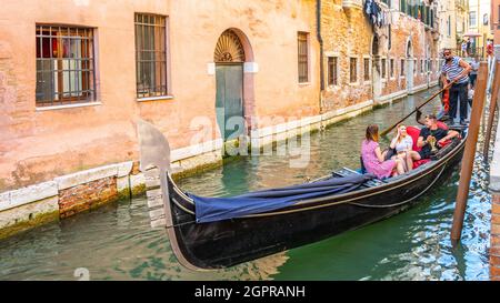 VENICE, ITALY - AUGUST 02, 2021: Tourists and gondolier on gondola boat. Romantic gondola cruise in Venetian water canal, Venice, Italy. Stock Photo