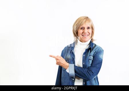 Mature smiling woman in white background pointing with his hand. Image for backdrop or mockup. Copy space. Stock Photo