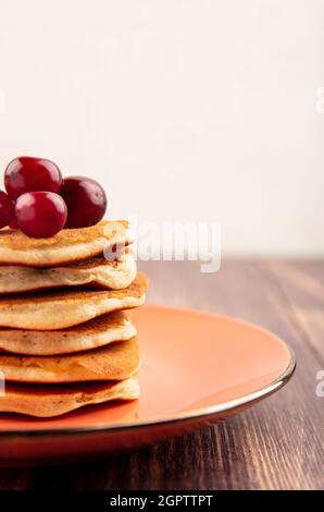 side view of pancakes with cherries in plate on wooden surface and white background Stock Photo