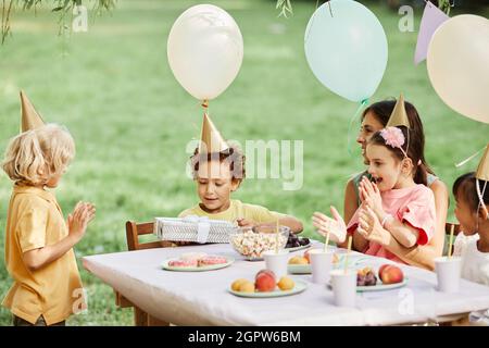 Side view portrait of group of kids enjoying outdoor Birthday party in summer and giving gifts Stock Photo