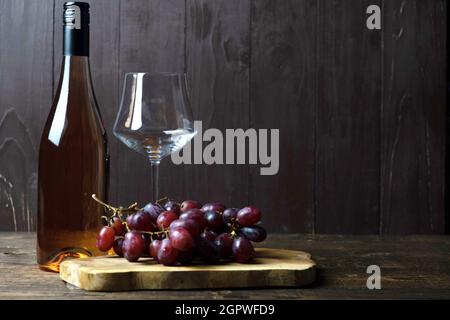A Bottle Of Rose Wine Stands On A Wooden Table, Next To An Empty Glass And A Bunch Of Grapes