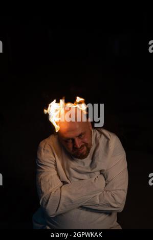 Bald man in a straitjacket with a burning head on a dark background. Stock Photo