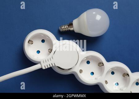 Energy saving bulb and power strip on blue background. Stock Photo
