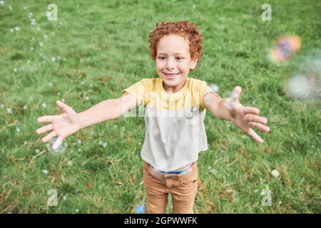Portrait of cute boy playing with bubbles outdoors in park and smiling, copy space Stock Photo