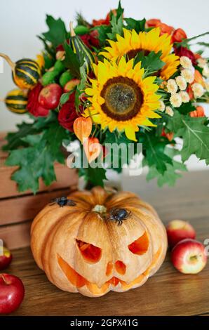 Autumn concept: pumpkins, candles, sunflower, spiders and other attributes at the table as Halloween party theme background. Halloween orange pumpkin with evil scary face. High quality vertical photo Stock Photo