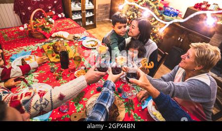 Happy multi generation family having fun at christmas supper party - New year's eve mood with group toasting red wine glasses - Winter holiday concept Stock Photo