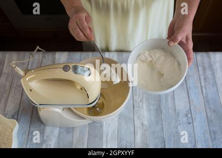 Step by step the process of making sour cream pie dough. Women's hands add sour cream to the mixer bowl for making dough. Baking concept. Stock Photo