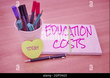 Handwriting text Education Costs. Business idea amounts paid for tuition fees and other related expenses Plain Blank Open Notebooks With Stack Of Pens Stock Photo