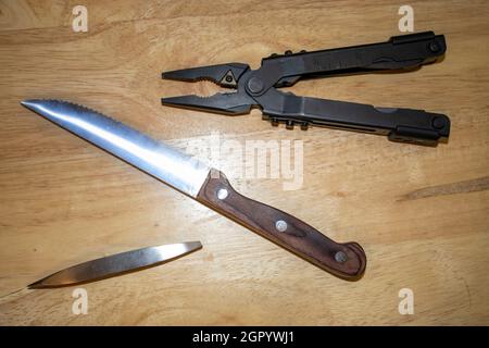 multitool steak knife and stainless steel tweezers on a light wood background Stock Photo