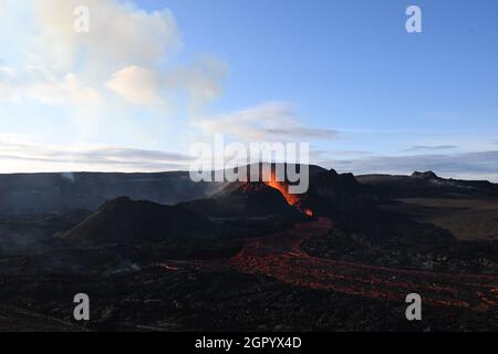 The lava field at Fagradalsfjall, Iceland. The active vent has orange molten lava erupting from it and white volcanic gas rising. Black lava field. Stock Photo