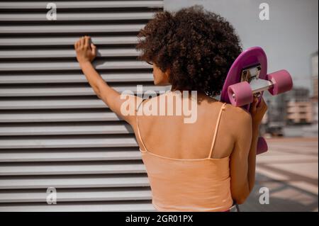 A curly-haired woman with a skateboard in hands Stock Photo