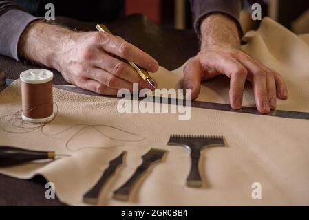 Shoemaker's male hands holding craft knife measuring leather before cutting in workshop. Closeup Stock Photo