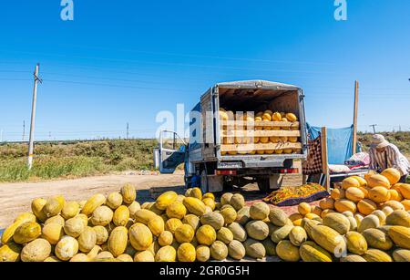 Man selling melons on the ground beside the full truck at the seasonal outdoor market in Kyzyl-Orda, Kazakhstan, Central, Asia Stock Photo
