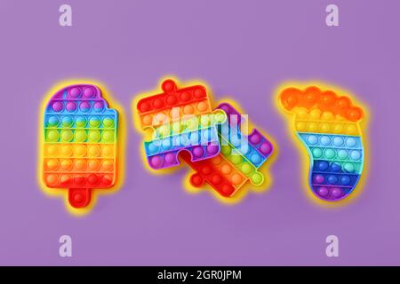 Colorful Push Pop It Bubble Sensory Fidget Toys of different shapes on purple background, top view Stock Photo