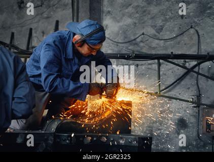 Competent locksmith using angle grinder during working process on industry. Caucasian man wearing protective uniform, gloves and glasses during danger Stock Photo