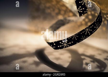 Abstract background with decorative black and gold ribbon with small dots in shape of flower or snowflake or star, twisted over gold lit background. Stock Photo