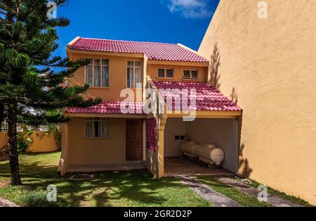 Full view of a beautiful two storied bungalow with ceramic tiled rooftop and yard protected by a high concrete wall on the side Stock Photo