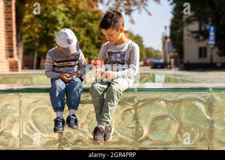 POZNAN, POLAND - Sep 05, 2021: Two young Polish boys sitting on a glass barrier and watching bugs in a jar Stock Photo