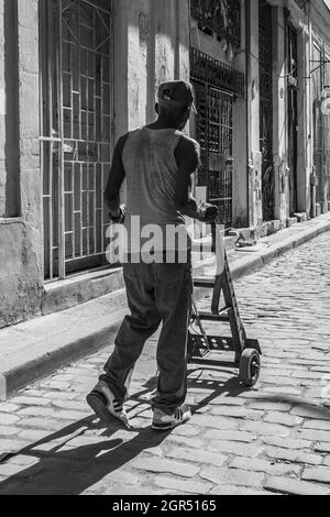 HABANA, CUBA - Jul 20, 2018: A grayscale shot of the old man walking on the street with a pushcart. Havana, Cuba. Stock Photo