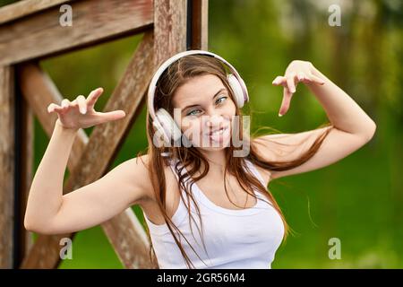 Woman 29 years old in wireless headphones is grimacing in park. Stock Photo