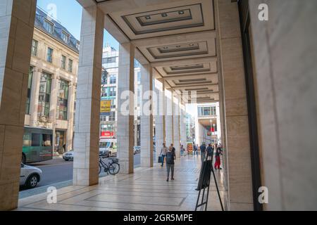 Berlin, Germany - August 28 2017; Portico of retail shops on city street with people blurred in motion walking along. Stock Photo