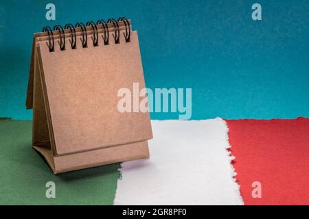 small, blank desktop calendar against paper abstract in colors of national flag of Italy (green, white and red), October is National Italian American Stock Photo