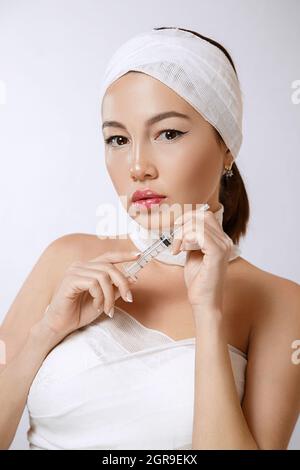 fashion portrait of a young beautiful Asian woman on an isolated background with a syringe in her hands. the syringe contains injections of drugs for Stock Photo