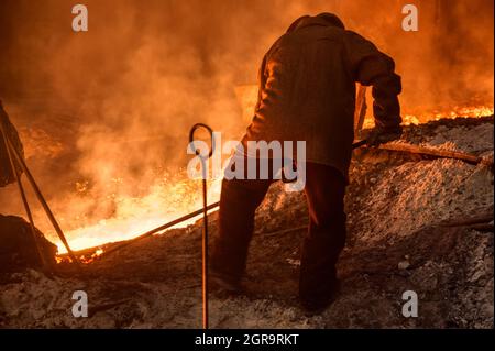 The process of releasing pig iron from a blast furnace. A man works with molten metal Stock Photo