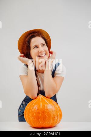 Farmer woman in overalls is enjoying the harvest with large pumpkin. Stock Photo