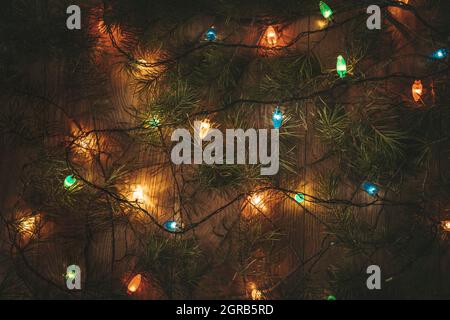 Christmas colorful lights and the green branches of the Christmas tree on wooden table Stock Photo