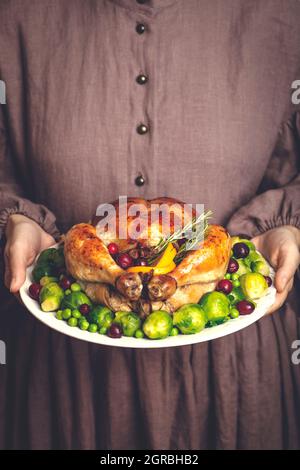 Thanksgiving turkey or chicken for a festive dinner. A plate of fried chicken in the hands of a woman in a classic American dress. Thanksgiving and autumn seasonal food concept. High quality photo Stock Photo