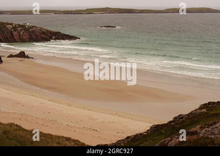 A view looking across Traigh Allt Chailgeag beach, Sutherland, Scotland, with a man walking along the beach Stock Photo