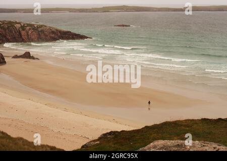 A view looking across Traigh Allt Chailgeag beach, Sutherland, Scotland, with two separate people walking along Stock Photo