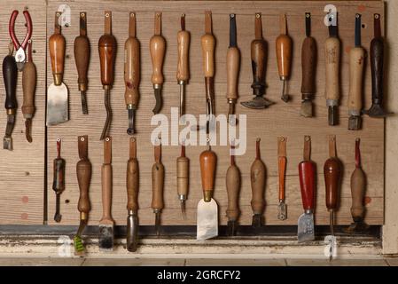 Set of leather craft tools hanging on the wall in workshop. Workplace for shoemaker. Various handmade shoemaking tools Stock Photo